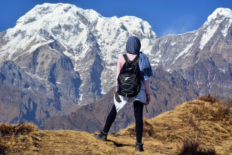 a woman traveller with a black bag-pack facing the snow-peak mountain